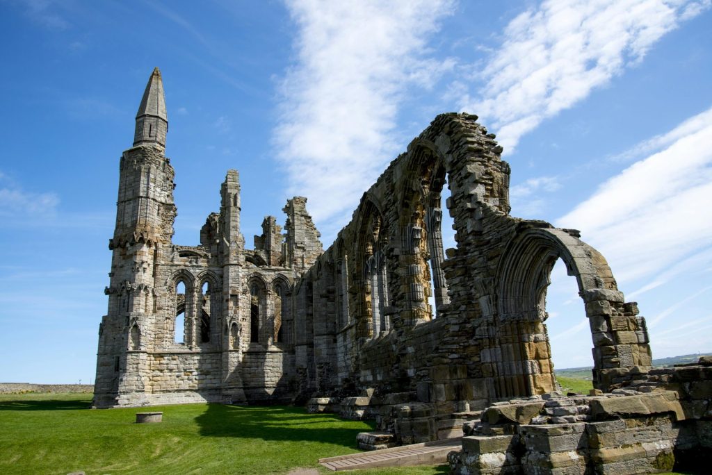 Explore the historic Whitby Abbey ruins against a vibrant blue sky, showcasing medieval architecture.